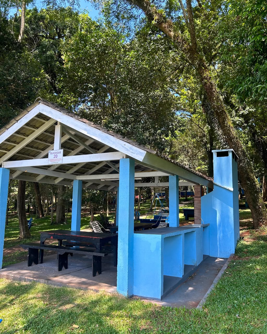 Quiosque do Grêmio Industrial Patobranquense com churrasqueira e mesa, sob as árvores