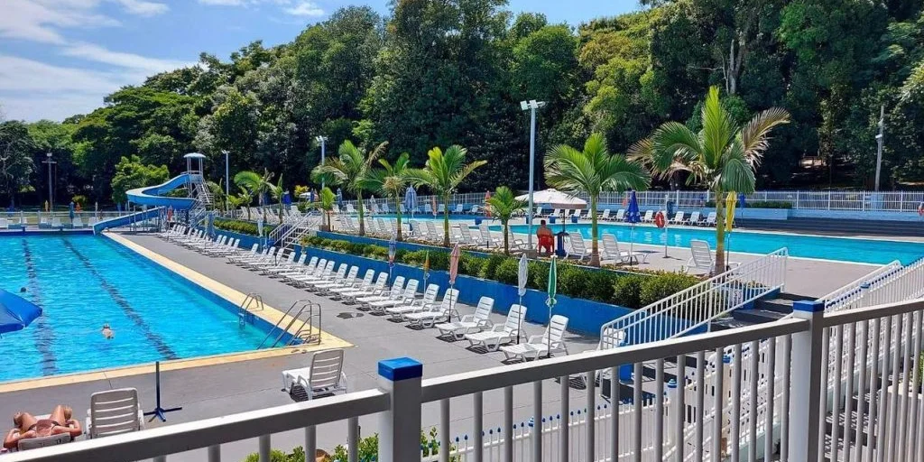 Piscinas do clube com espreguiçadeiras e palmeiras em dia de sol